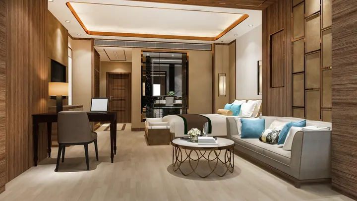 A hotel suite with a work desk, a sofa and a bed beyond