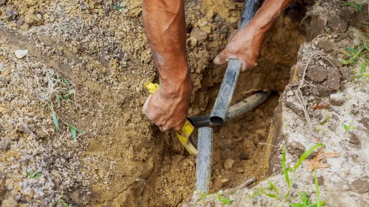 A worker's hands joining a pipe down in a dirt trench